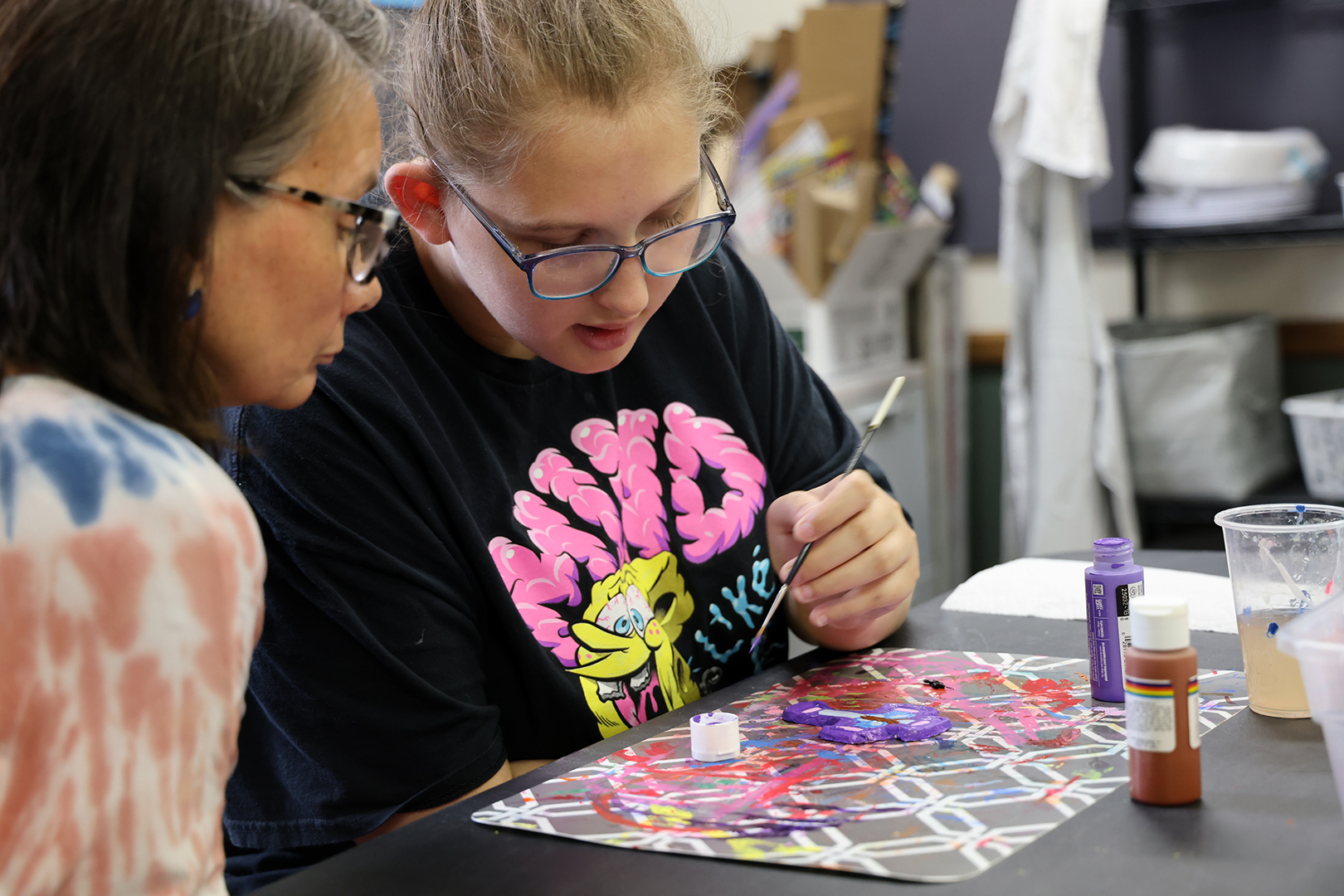 Zoe Johnson paints a wooden cross with the help of an Our Place teacher. Photo by Russell Shaffer