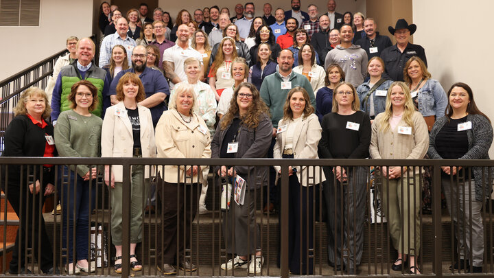 Group photograph of people standing on staircase, smiling in a brightly lit indoor setting.