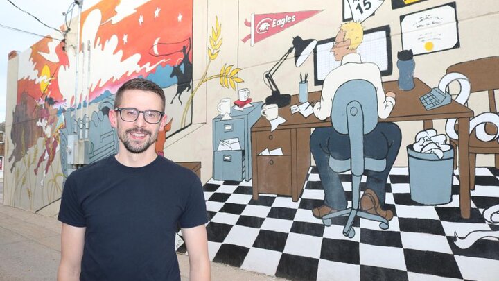 Travis Hencey stands in front of “Beating the Deadline,” the newest mural he designed for Chadron’s Art Alley.