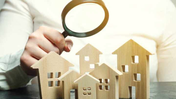 Stock photo of someone holding a magnifying glass up to toy wooden houses.