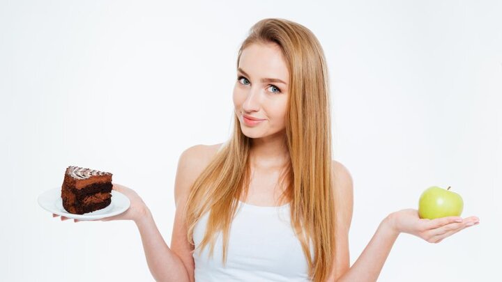 Stock photo of attractive woman holding healthy and unhealthy food.