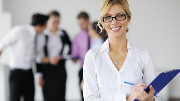 Stock photo of business woman standing with staff in background.