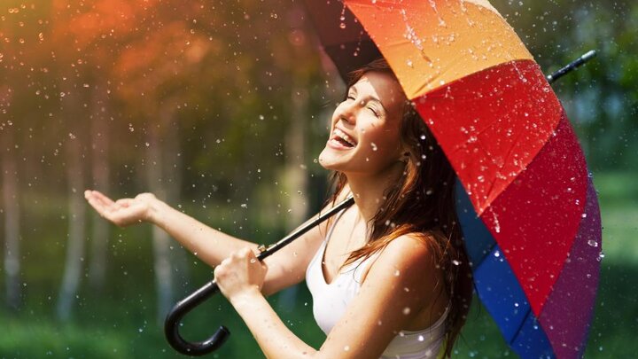 Stock photo of laughing woman with umbrella checking for rain.