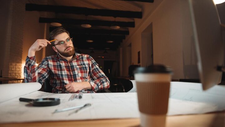 Stock Photo of Pensive Bearded Man Sitting At His Working Place With Graphs And Cup Of Coffee