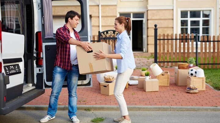 Stock photo of man taking cardboard boxes out of moving van and passing them to his wife. Photographer unknown.