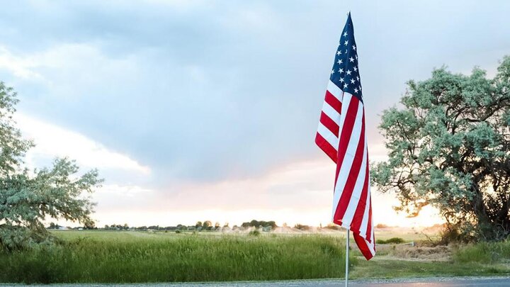 Photo of American flag in front of a green field. Photo by Saydee Longhurst