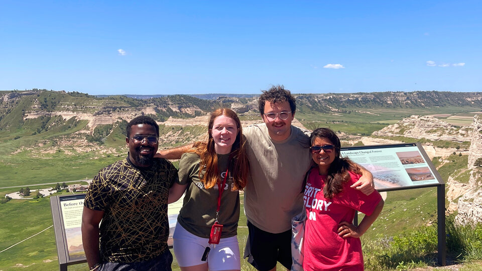Four Rural Fellows students stand arm in arm in front of a scenic viewpoint outside Sidney, Neb.