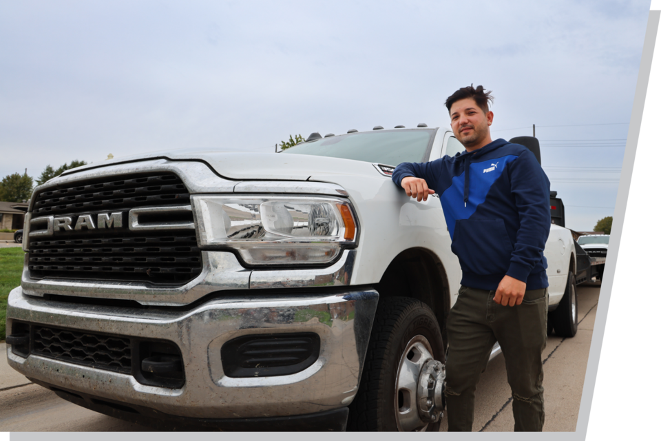 Joes Yera leans against a white Dodge Ram, one of the trucks he uses as part of his transportation business.