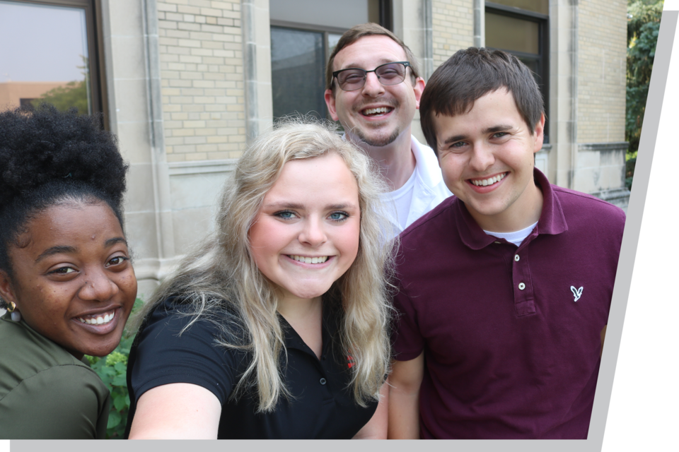 Students crowd together and smile while taking a selfie.