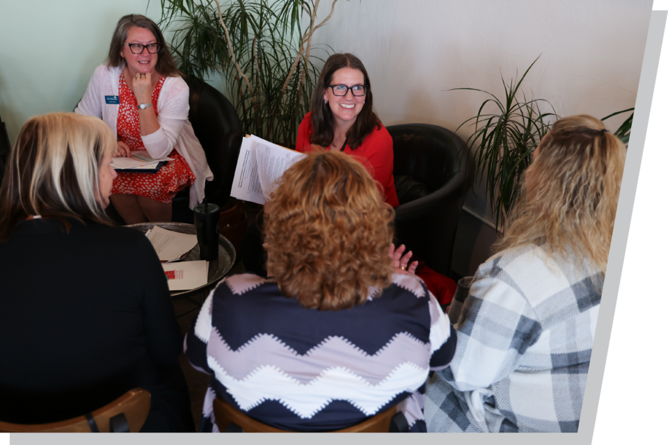 Two female Extension educators talk with a group of other woman in the gathering area of an office.