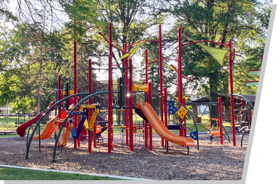 A playground at a city park on a sunny day, with leafy, green trees in the background.