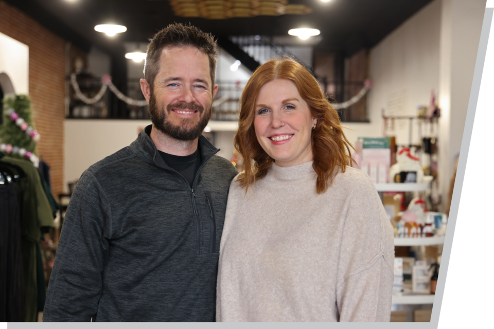 A man and woman stand side by side, smiling at the camera, inside the boutique they own.