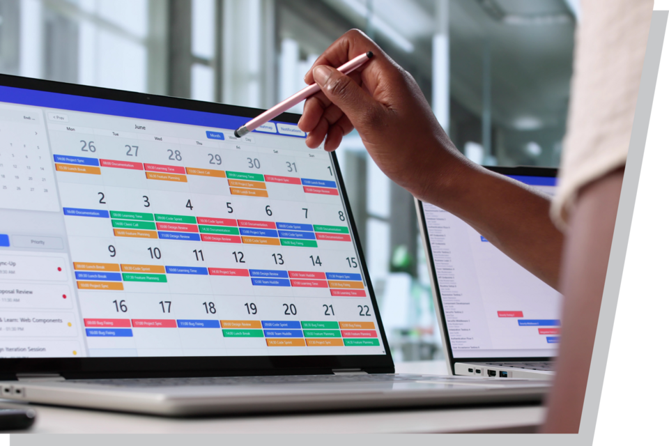 Digital calendar displayed on a laptop, hand pointing with a stylus, modern office in the background.