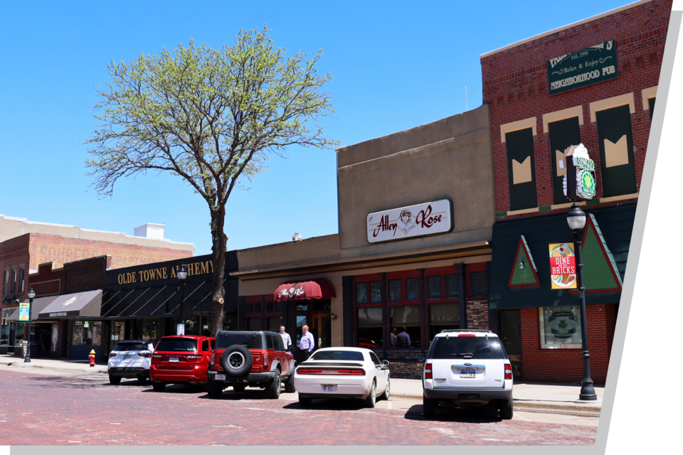 A small-town Main St. view of small businesses with cars parked in front.