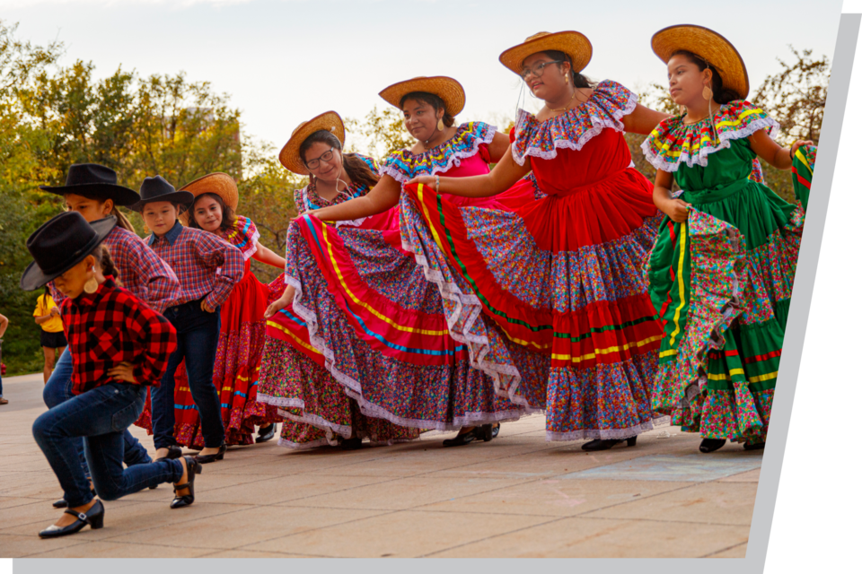 Dancers in colorful traditional dresses and hats performing outdoors, with vibrant fabric details.