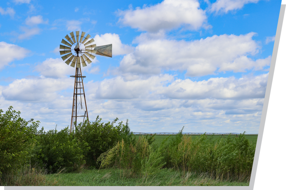 A windmill in a green field with a blue sky and clouds in the background.