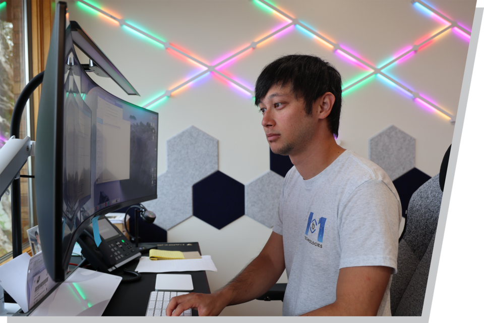 A man working on a computer, looking at his monitor, with neon lights in the background.
