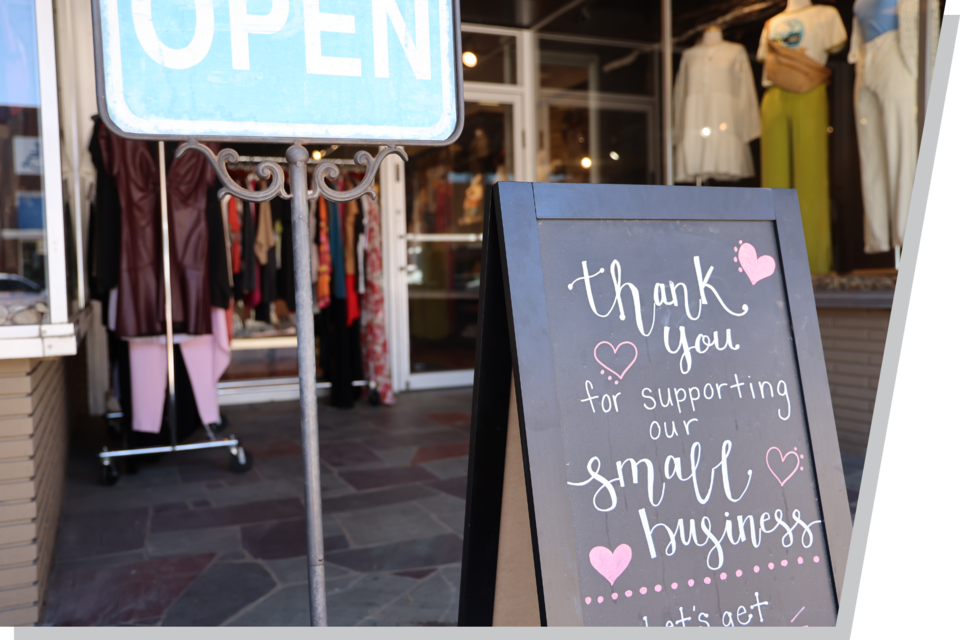 Two signs in front of a small clothing shop. One reads "Open," and the other reads, "Thank you fro shopping at our small business."